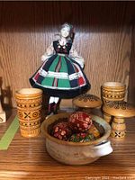 Photo shows doll in native costume behind two decorated wooden cups, wooden mushrooms, and ceramic dish with painted eggs
