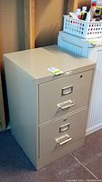 Front view of the beige two-drawer metal file cabinet showing handles, label holders, and lock on top drawer.