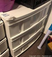 White plastic organizer with three drawers placed on floor next to other items.
