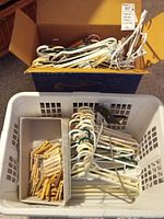 Box of assorted plastic hangers with different colors, including white, green, and yellow. White plastic over-door hanger placed in plastic laundry basket.