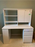 Front view of the white desk with three drawers, open shelves, and the hutch on top showing the locked cabinet with key