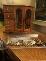 Jewelry box with stained glass doors and four drawers with costume jewelry in a plastic bag in front.
