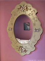 Full view of oval mirror with floral painted frame showing reflection and mounted bicycle print in background