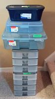 Stack of plastic organizer drawers topped with Rubbermaid snap cases and a black shoebox.