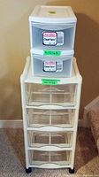 Front view of the white plastic storage organizer with four clear drawers on black caster wheels, topped by two Sterilite single-drawer units.