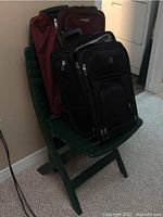 Photo showing two wheeled suitcases placed on a green folding chair against a wall near laundry appliances.