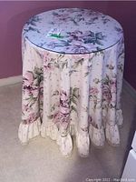 Occasional table covered with floral fabric tablecloth and glass top, showing ruffled edge detail.