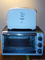 White Hamilton Beach toaster placed on top of black Black & Decker toaster oven showing front and side views