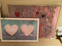 Two framed abstract heart-themed paintings, one large canvas with multiple hearts and one smaller with two pink hearts