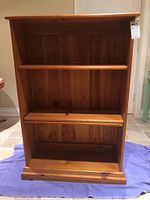 Front view of wooden bookcase showing natural wood grain and three shelves, one positioned as middle shelf, two lower shelves, and vertical panel backing.