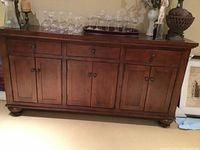 Front view of medium brown wooden buffet with three drawers above six cabinet doors, bun feet and metal knob hardware