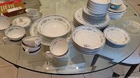 Full view of Mikasa Roslyn pattern cups, bowls, and plates on a glass table