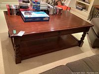 Full view of the rectangular heavy wood coffee table with turned legs and drawer, showing scratches on surface and contents on top excluded from sale.