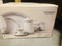 Photo of Tienshan Fine China box showing 47-piece set contents and floral design pattern on dishes.