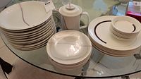 Stack of 9 white Wedgwood plates and 8 bowls with rainbow stripe design, along with a white ceramic pitcher with lid on a glass table