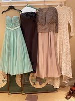 Four evening gowns hanging on a rack, displaying different styles and colors