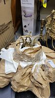 Hanging light fixture wrapped in brown and white packing paper, shows the main metal frame and hanging crystal strands.