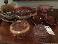 Overview of various cranberry glass bowls, lidded dishes, and ceramic pieces on a wooden surface