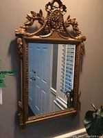 Full view of the rectangular mirror hanging on a wall showing carved wooden frame in gold color and reflective surface.