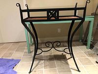 Front view of the vintage metal planter showing the rectangular rusted tray and curved legs with scroll details.