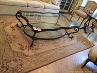 Living room scene showing the full embroidery rug under a glass coffee table and sofa, highlighting the rug's color and floral design.