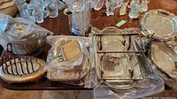 Photo of various silverplate items including trays, teapot, toast holder, and serving dishes arranged on a wooden table.
