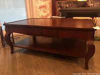 Front view of dark wooden coffee table with two drawers and lower shelf, showing cabriole legs and polished finish.