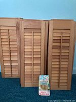 Three pairs of wooden shutter panels leaning against wall with floor sample.
