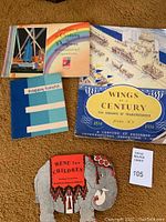 Four items displayed on carpet: "Wings of a Century" Chicago World Fair booklet, illustrated brochure, blue "happy hours" booklet, and elephant shaped children's menu