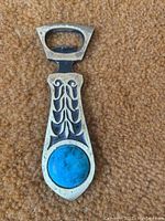 Photo of metal bottle opener showing ornate Art Nouveau style design with a large turquoise-colored stone on the handle.