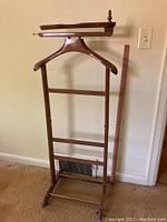 Full view of the wooden clothing valet showing its overall structure with hanger, horizontal bars, and casters.