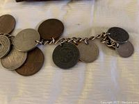 Close-up photo of the coin bracelet showing multiple attached coins of different sizes and metal tones on a chain.