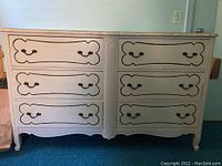 Front view of French Provincial style dresser, showing 6 drawers with decorative trim and handles, painted white with distressing.