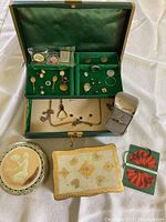 Green jewelry box open showing pins, earrings, a watch, bracelets, and a ring.