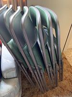 Stack of seven metal folding chairs with green vinyl padded seats and backs.