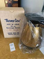 Image of the Thermo-Serv beverage carafe wrapped in plastic showing gold body, black handle and lid, and original cardboard box with blue text.