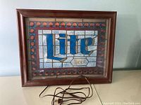 Full view of the Miller Lite electric light sign with wooden frame and electric cord on surface.