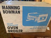 Box of Manning Bowman Deluxe Combination Oven Broiler with printed product image and branding on top of a table.