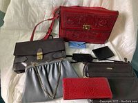 Overall group of seven ladies bags and wallets shown on a white background, includes red tooled leather handbag, multiple smaller wallets and purses of black, gray, blue, and red colors.