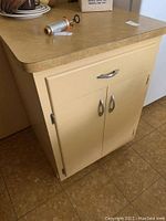 Full view of harvest gold retro kitchen island with laminate countertop, drawer and two-door cabinet, showing metal handles and surface.