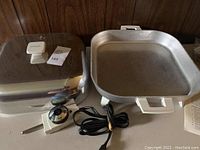 Square Sunbeam electric fry pan with removable lid, temperature control dial, and electrical cord, shown fully assembled separately on wood background.