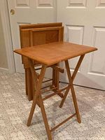 Image showing three wooden TV tray tables folded and stored in matching wooden storage rack against a white door background.