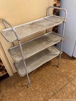 Full view of three-tiered aluminum bar cart with wear visible on trays.