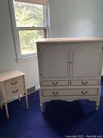 Full view of vintage cream armoire and matching nightstand in a room with blue carpet and light walls