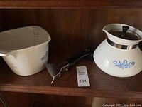 Photo showing white Corning Ware Cornflower Blue 4 cup sauce maker with handle and spout alongside the matching 4 cup coffee pot with black knob lid and metal rim.