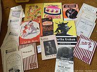 Top view of various vintage playbills and concert programs including Oklahoma!, Carousel, Call Me Mister, and others arranged on a brown surface.