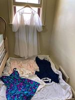 Full view of the nightgown and peignoir hanging, and various garments laid below on the floor