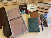 Wide shot showing all accessories included in the lot placed on a wooden surface, featuring the Pierre Cardin muffler in original packaging, ties, wallets, keychains, pens, lighter, and ashtray.