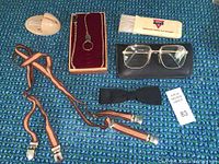 Photo showing a striped suspender, black silk bow tie, gold framed eyeglasses with case, Hickok pocket watch chain in box, and YMCA shoe and suit cleaning brush.