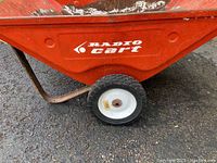 Close-up of one side of cart showing Radio Cart logo on red metal bucket and a white wheel with black rubber tire.